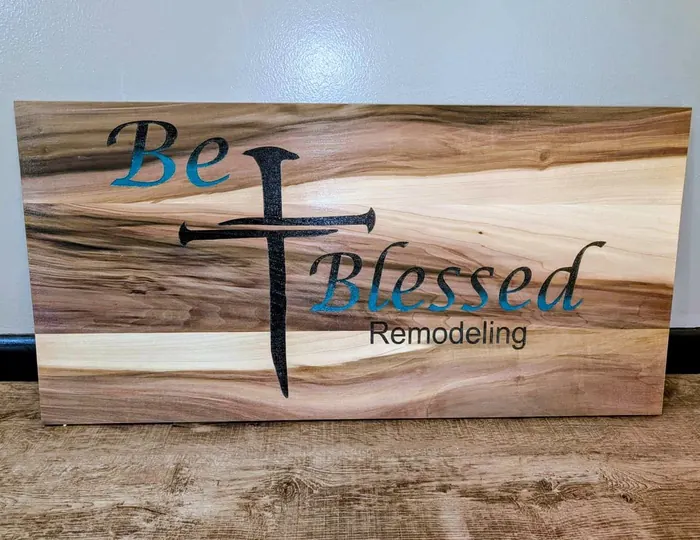 Poplar wood sign with a black and blue Be Blessed Remodeling logo over natural wood grain.
