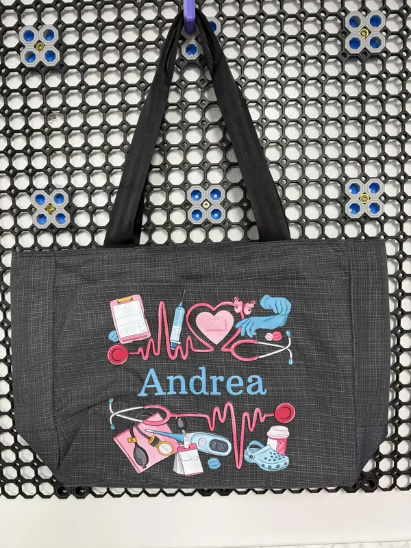 Black tote bag personalized with Andrea’s name and colorful nursing graphics, including stethoscopes and a heartbeat line.