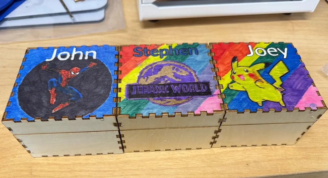 Three wooden keepsake boxes with finger-jointed corners, colorful illustrated lids, and personalized names.